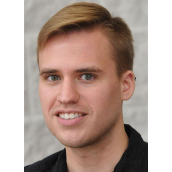 White man with short blond hair swooped to the right side, wearing a black polo shirt.