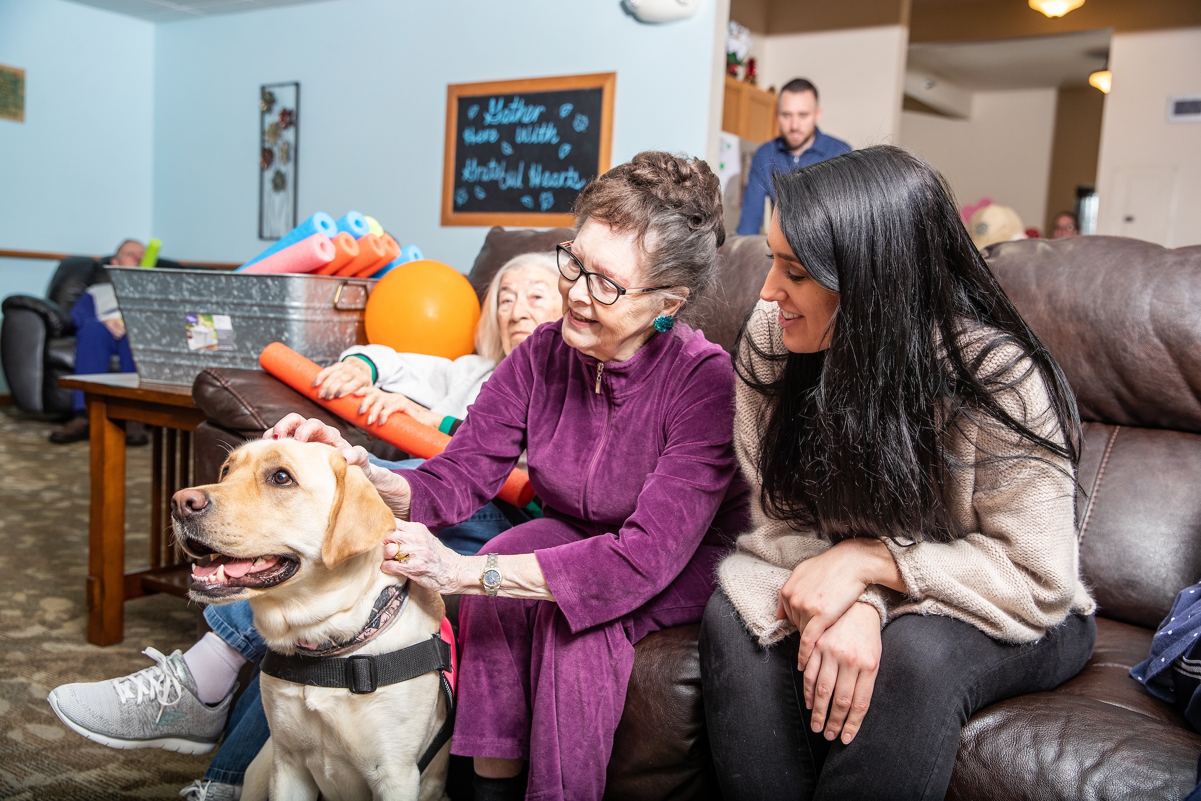 A graduate student and a older adult woman pay attention to a therapy dog.