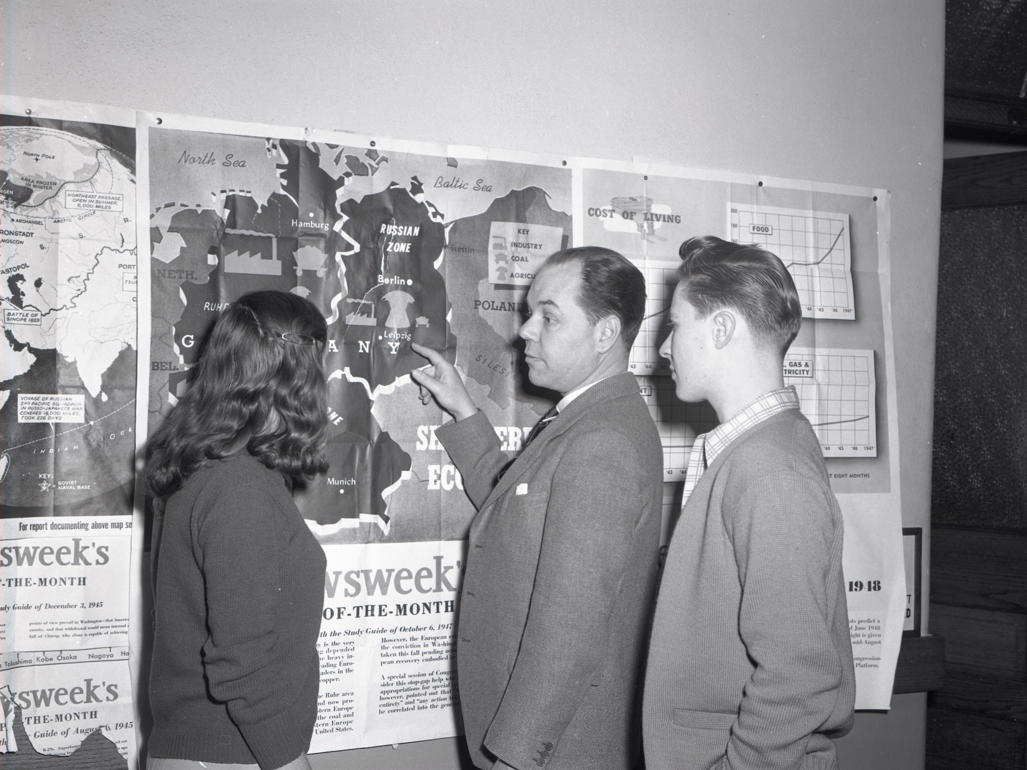 A professor, likely Lyman Harris, showing two students a map of Germany mounted on the wall. The original description included "Social Science: Dr. Harris and students" 1948
