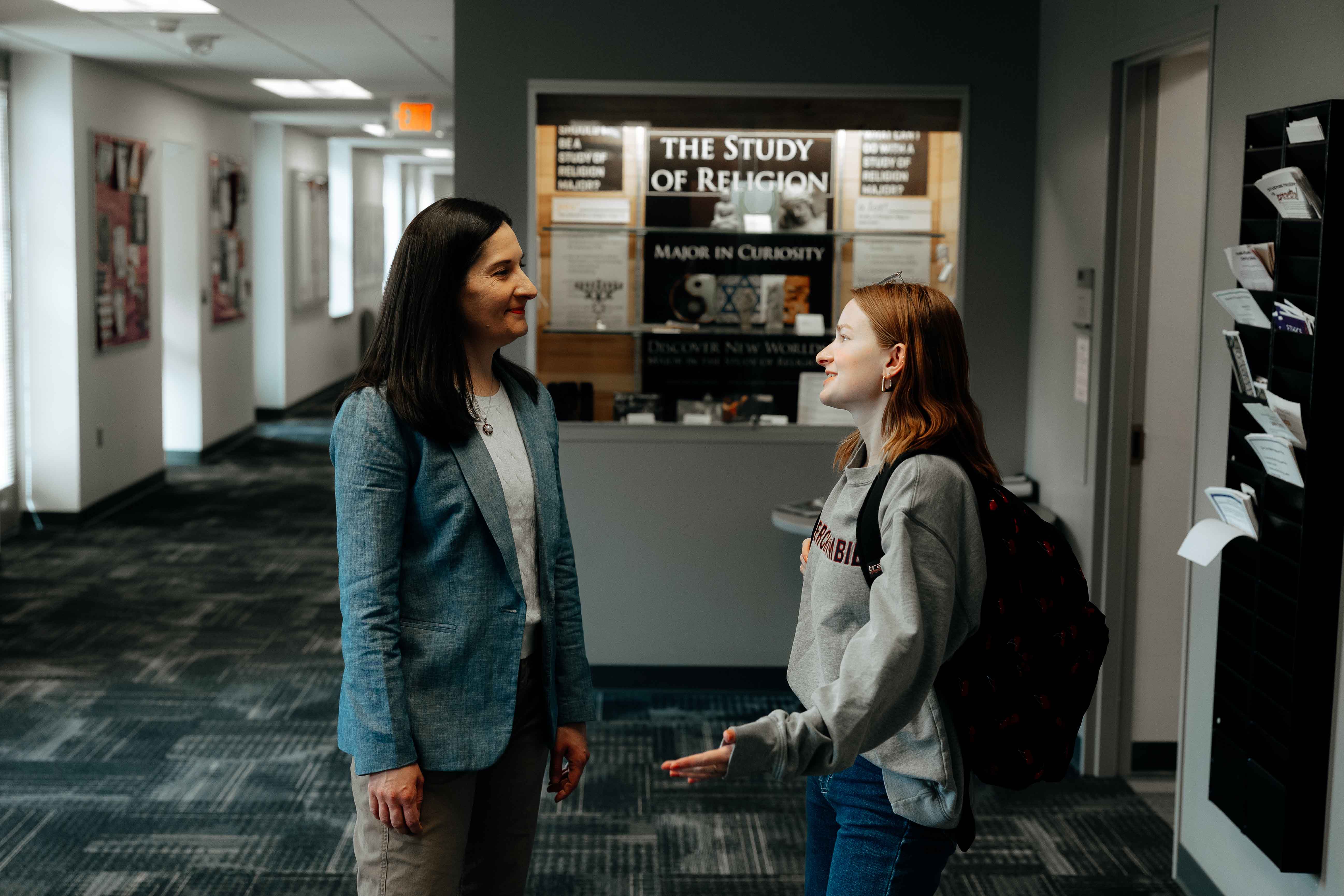 Student standing in hallway having conversation with professor