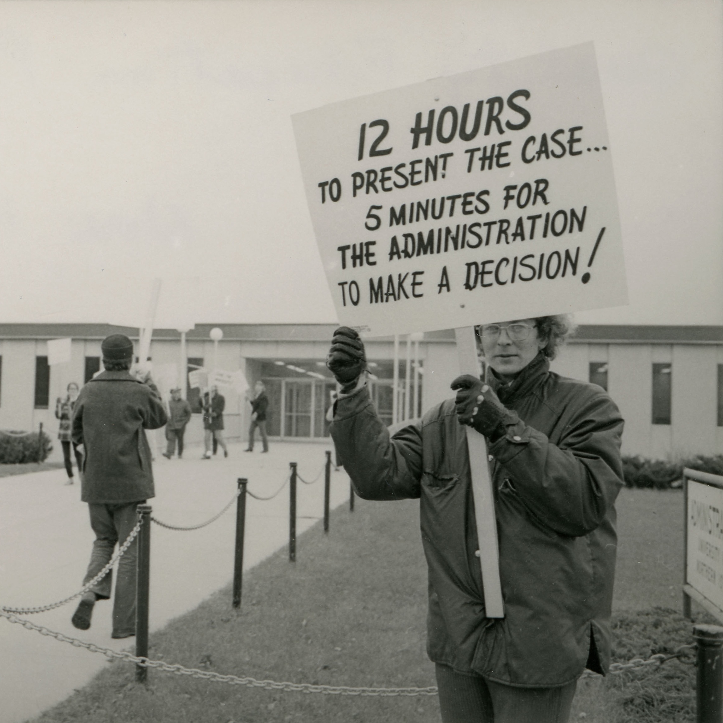 Student holding "12 hours to present the case ... 5 minutes for the administration to make a decision" sign outside Gilchrist Hall.“FI0019016,” UNI in CF, 1976 by UNI Special Collections & University Archives/Fortepan IA